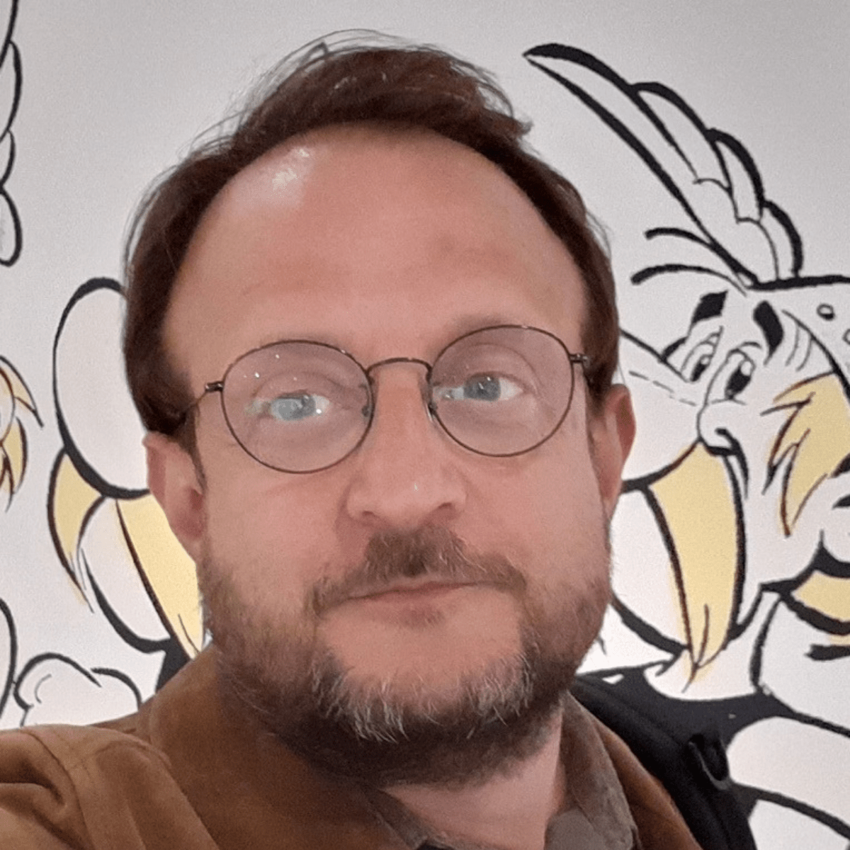 Photo d'un homme avec des lunettes et un dessin d'Asterix derrière lui
