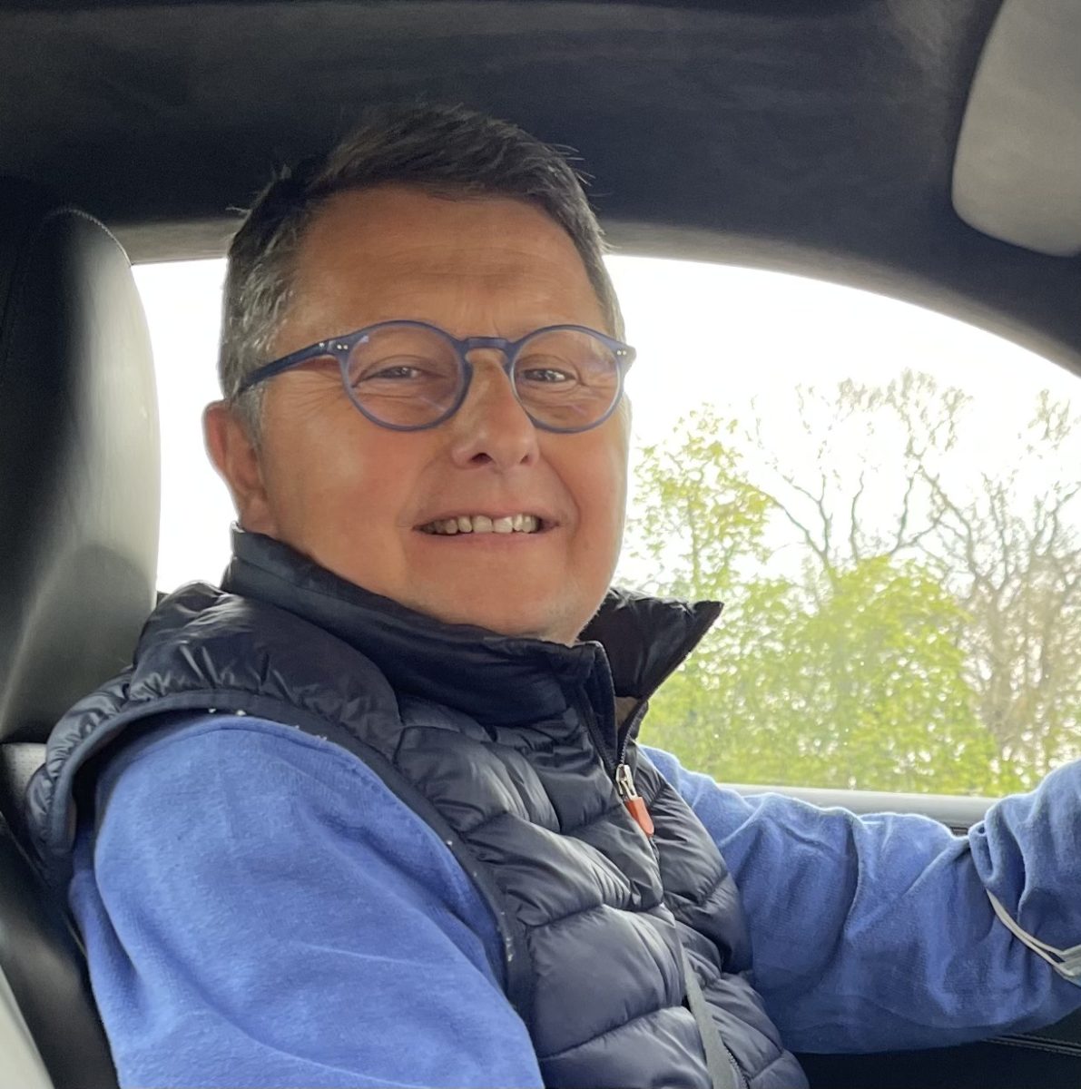 Homme souriant d'un certain âge avec des lunettes au volant de sa voiture